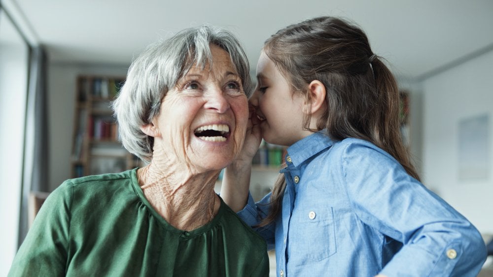 Young girl whispering in her Grandma's ear