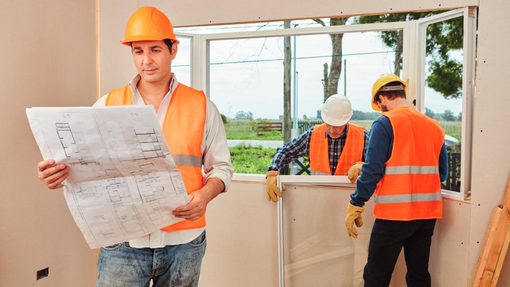 Builder looking at plans while window is being fitted