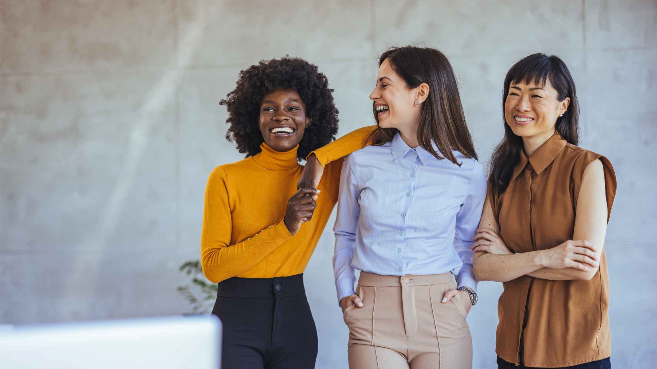 A diverse group of three women smiling and enjoying each other's company in a modern office environment