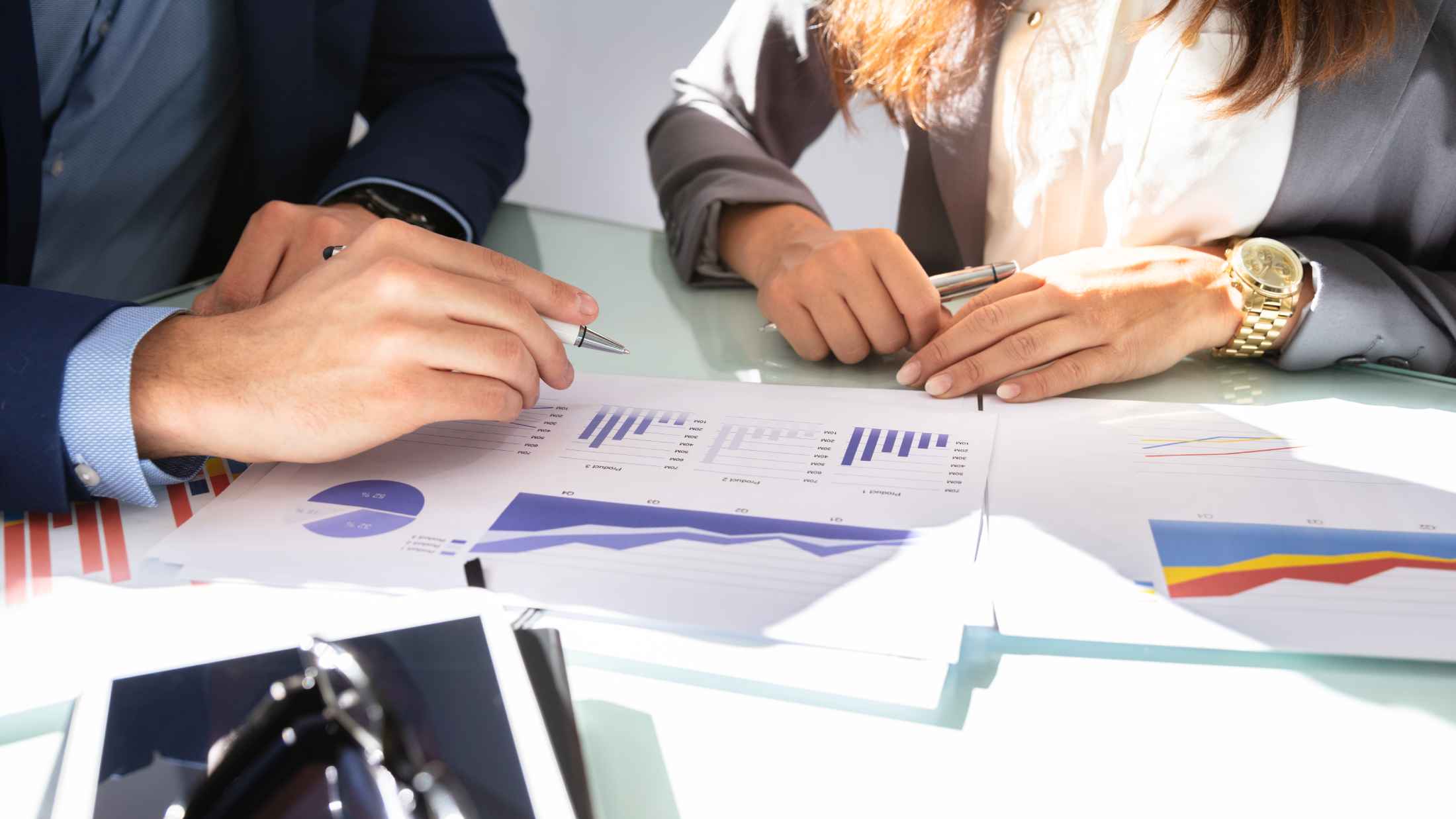 Close-up of two businesspeople's hand analysing graph on desk in office