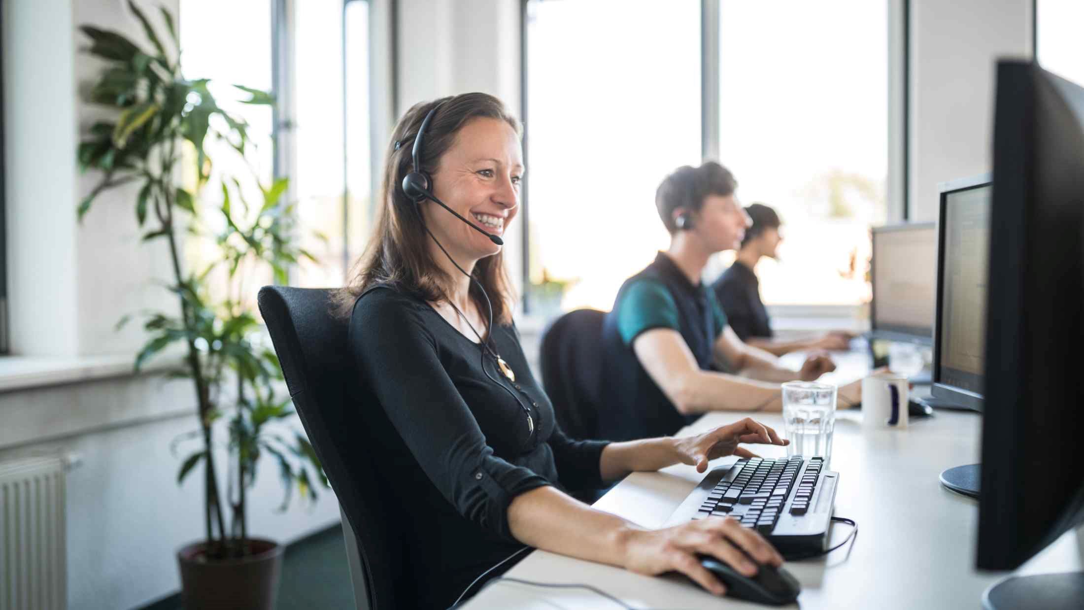 Smiling female customer service representative wearing headset and using computer at desk