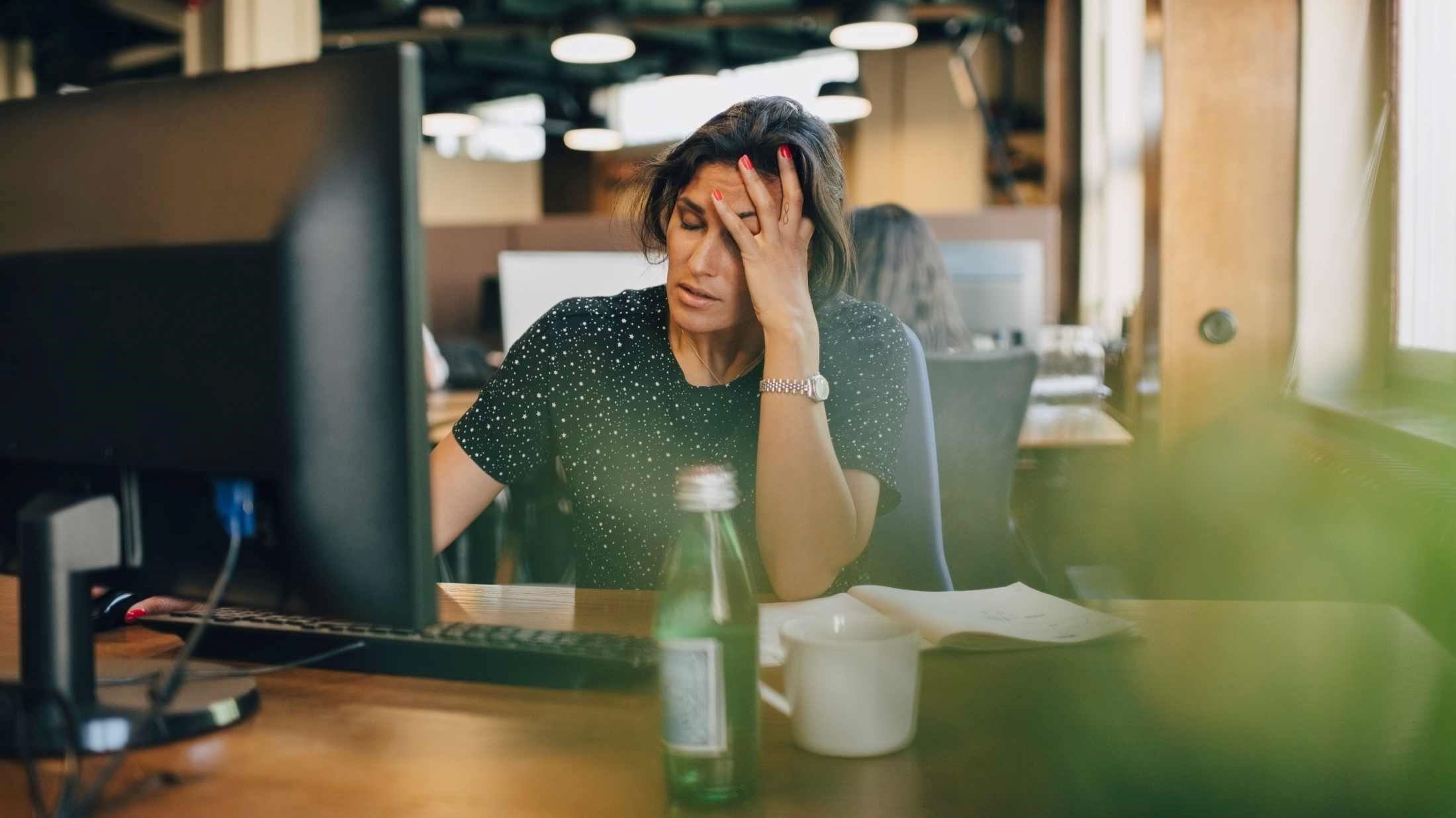 Tired businesswoman with head in hand sitting at computer desk in office