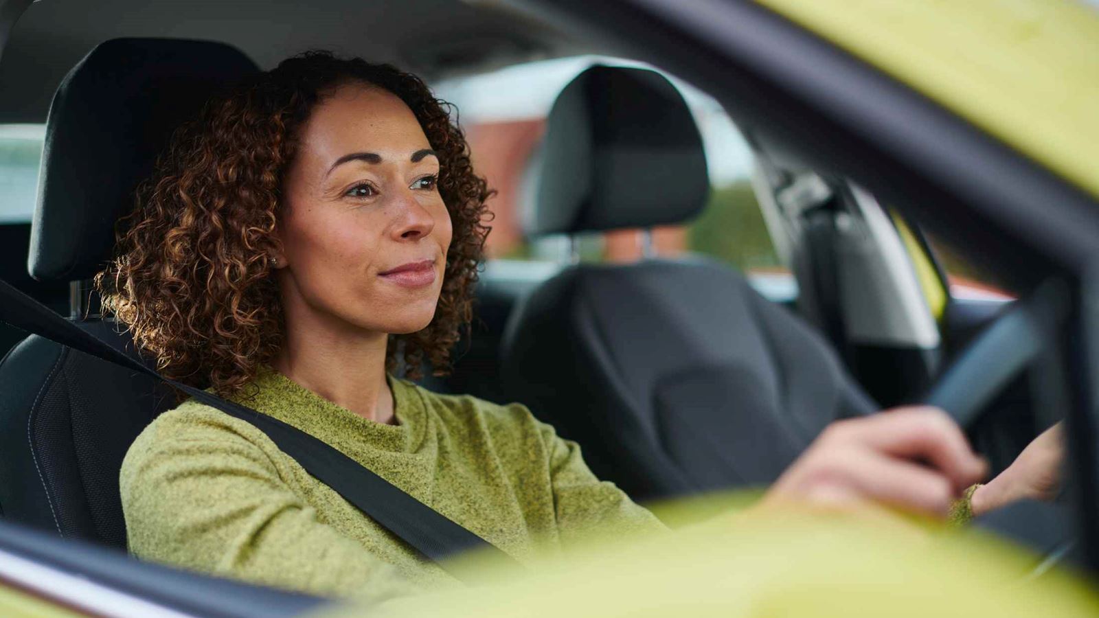 Woman wearing a green jumper driving a green car