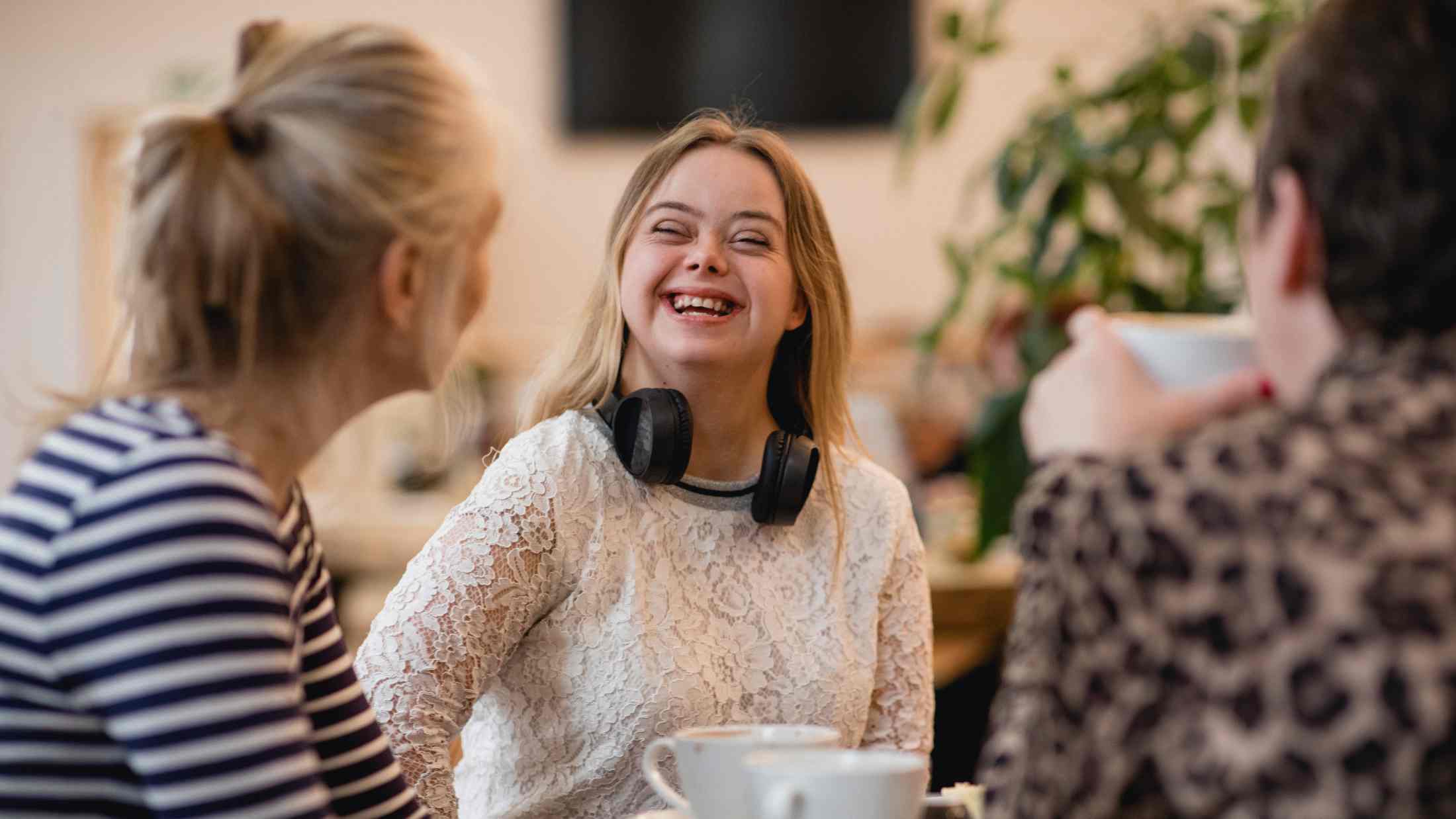 Young female adult with downs syndrome sitting in a cafe relaxing and laughing with friends