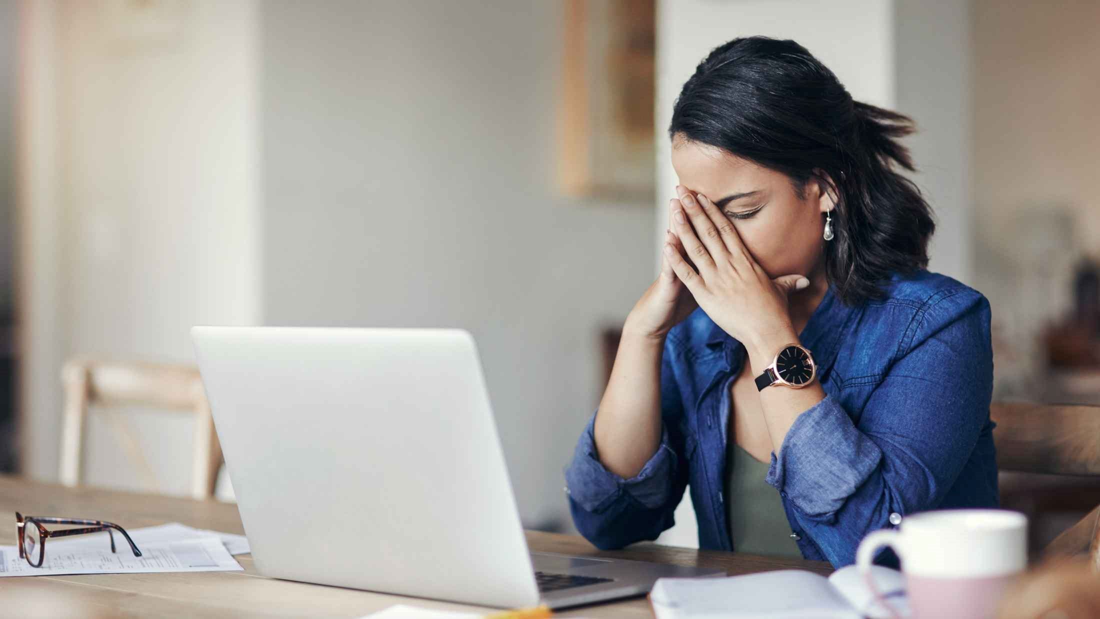 Young woman looking stressed while using a laptop to work from home