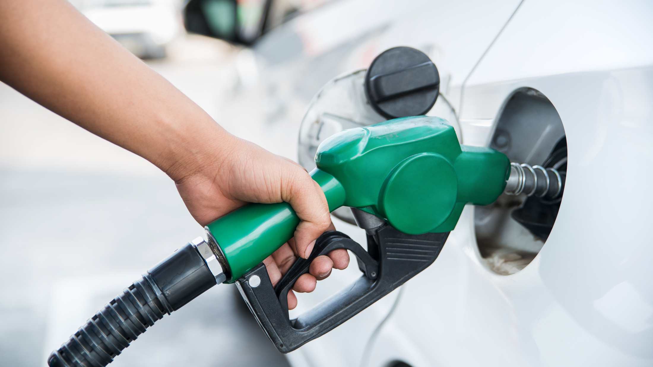 Hand holding refuelling nozzle inserted into a white car