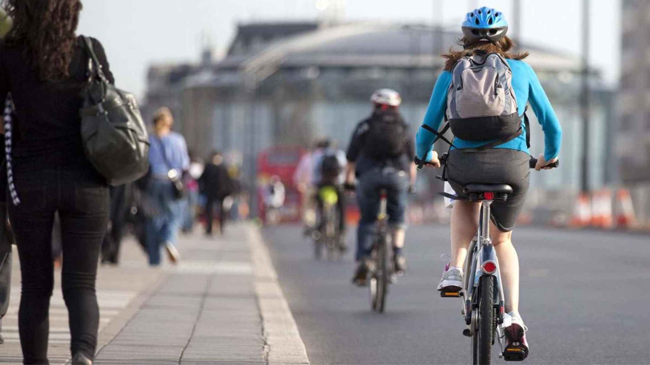 Woman wearing blue top and blue helmet cycling towards central London