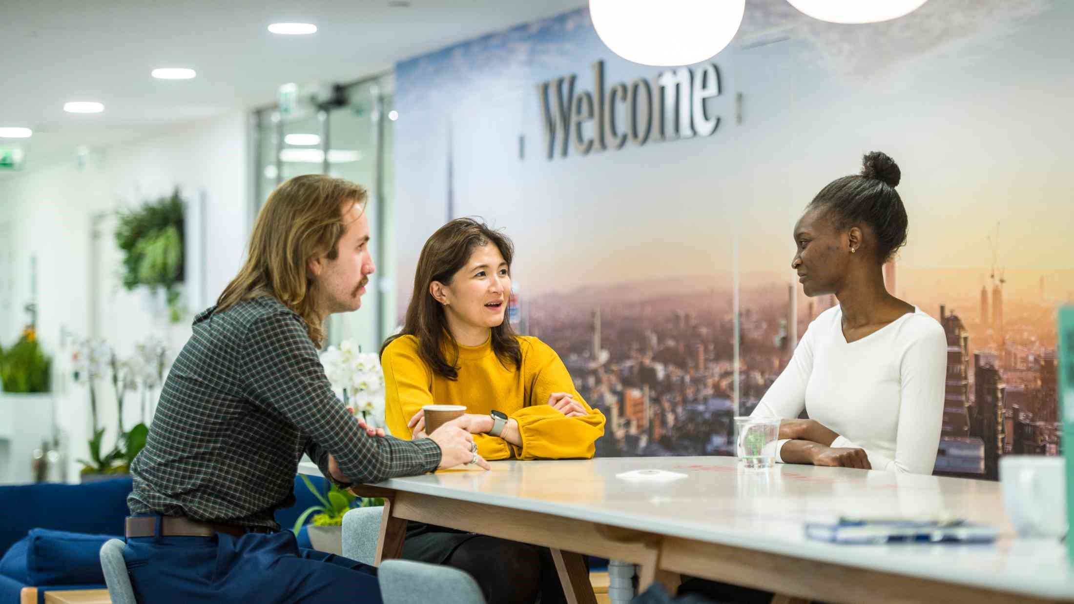 Colleagues in an AXA office sat round a high table with Welcome sign in the background