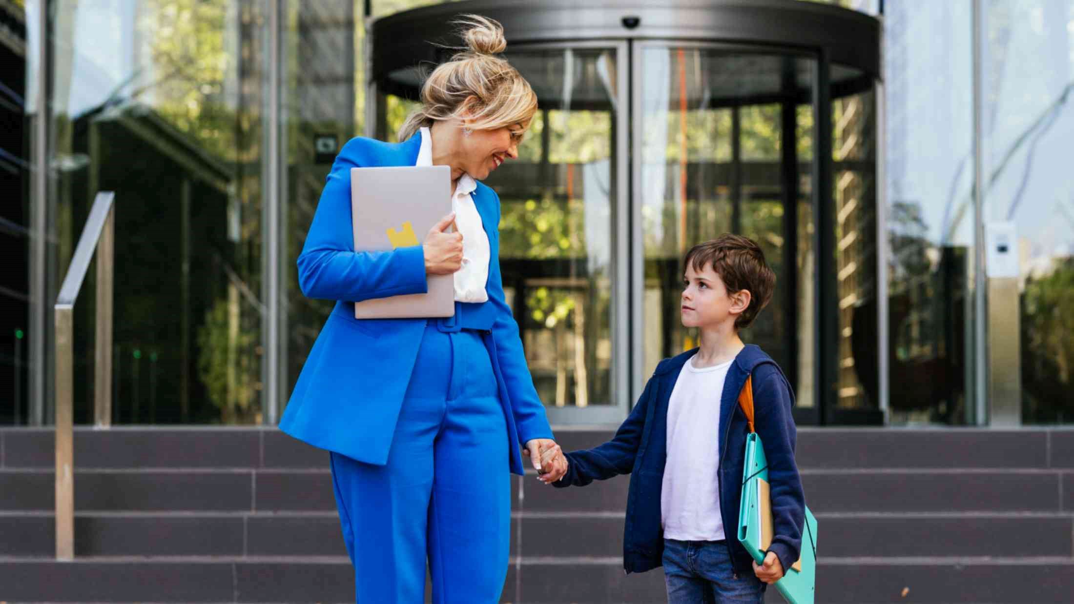 Working mother holding her sons hand outside a corporate office building