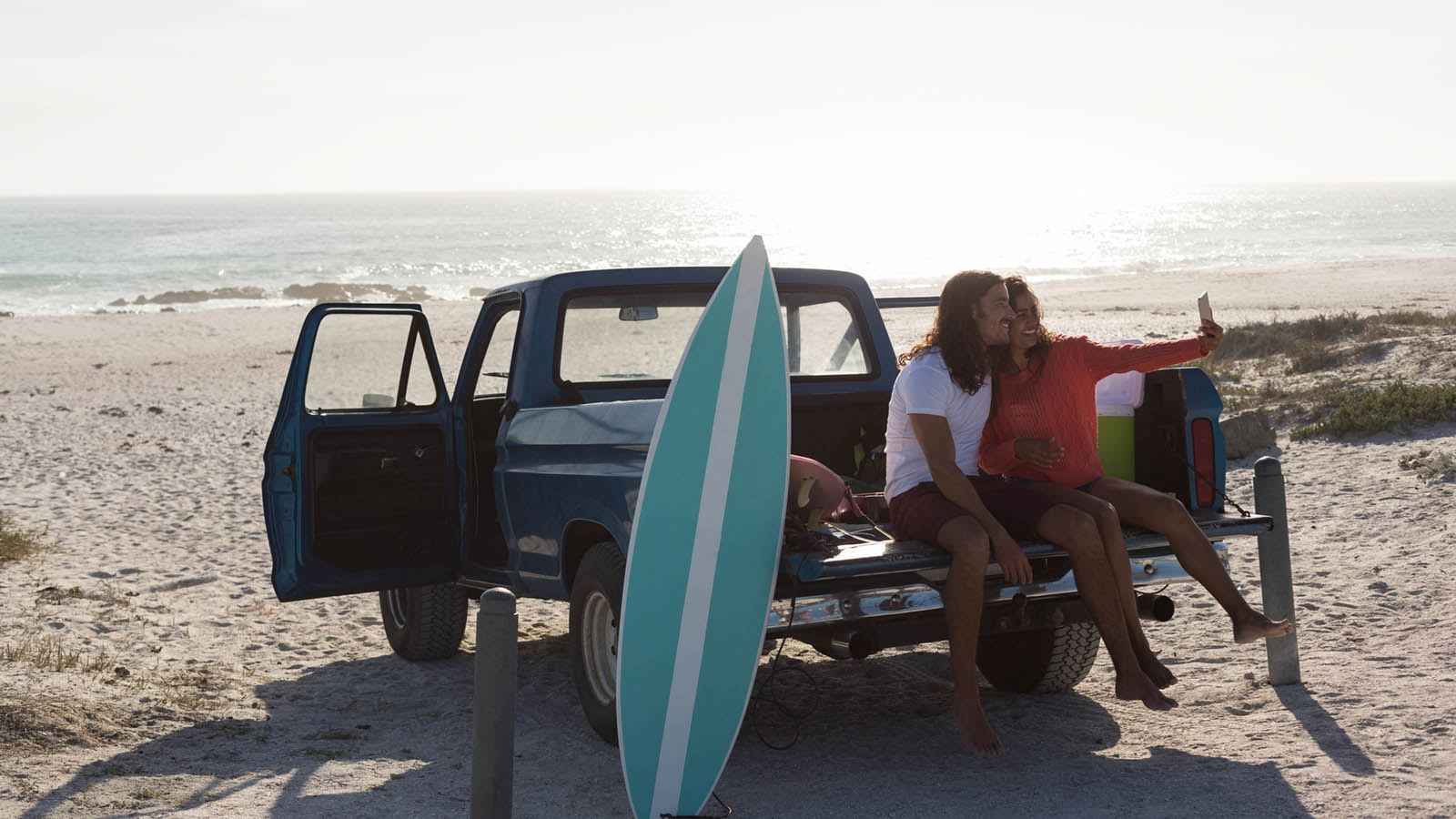 Couple taking a selfie on the beach while sat on the back of a pickup truck