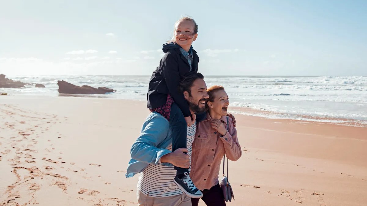 Family walking along the beach with daughter on her dads shoulders
